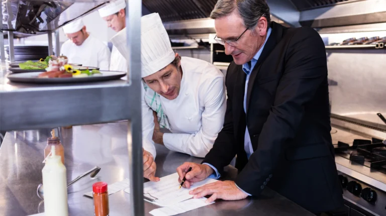 Chef and restaurant manager reviewing paperwork together in a commercial kitchen