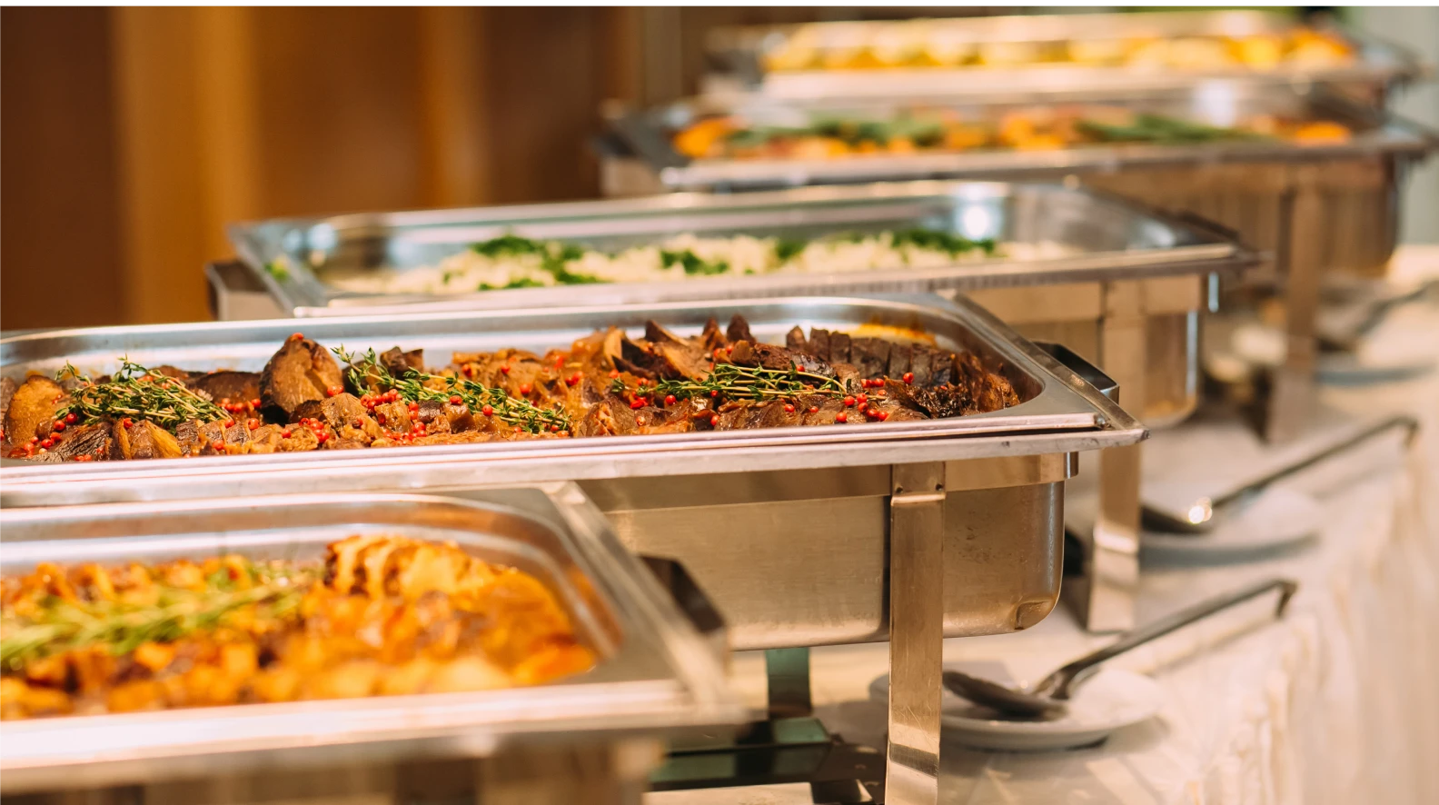 Buffet-style catering trays filled with hot food for a restaurant catering setup.