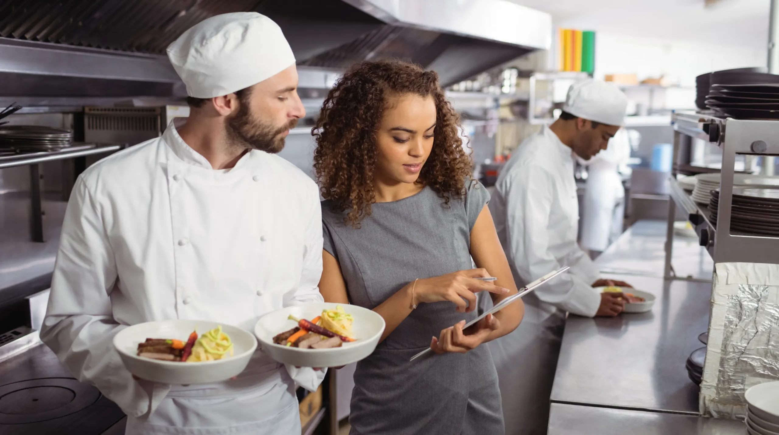 Restaurant manager reviewing kitchen operations and purchasing decisions with chefs in a commercial kitchen.